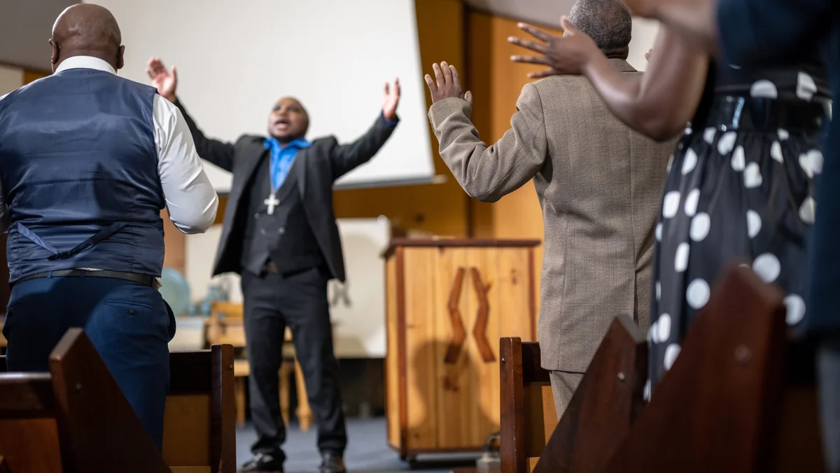 A pastor leading a congregation in prayer with hands raised