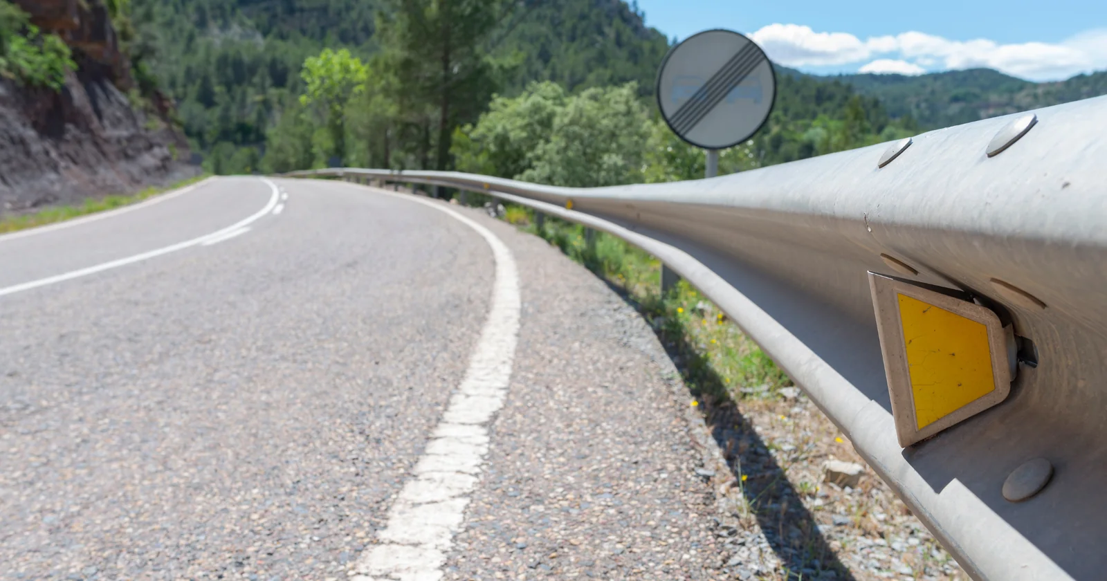 A metal highway guardrail curving alongside a mountain road