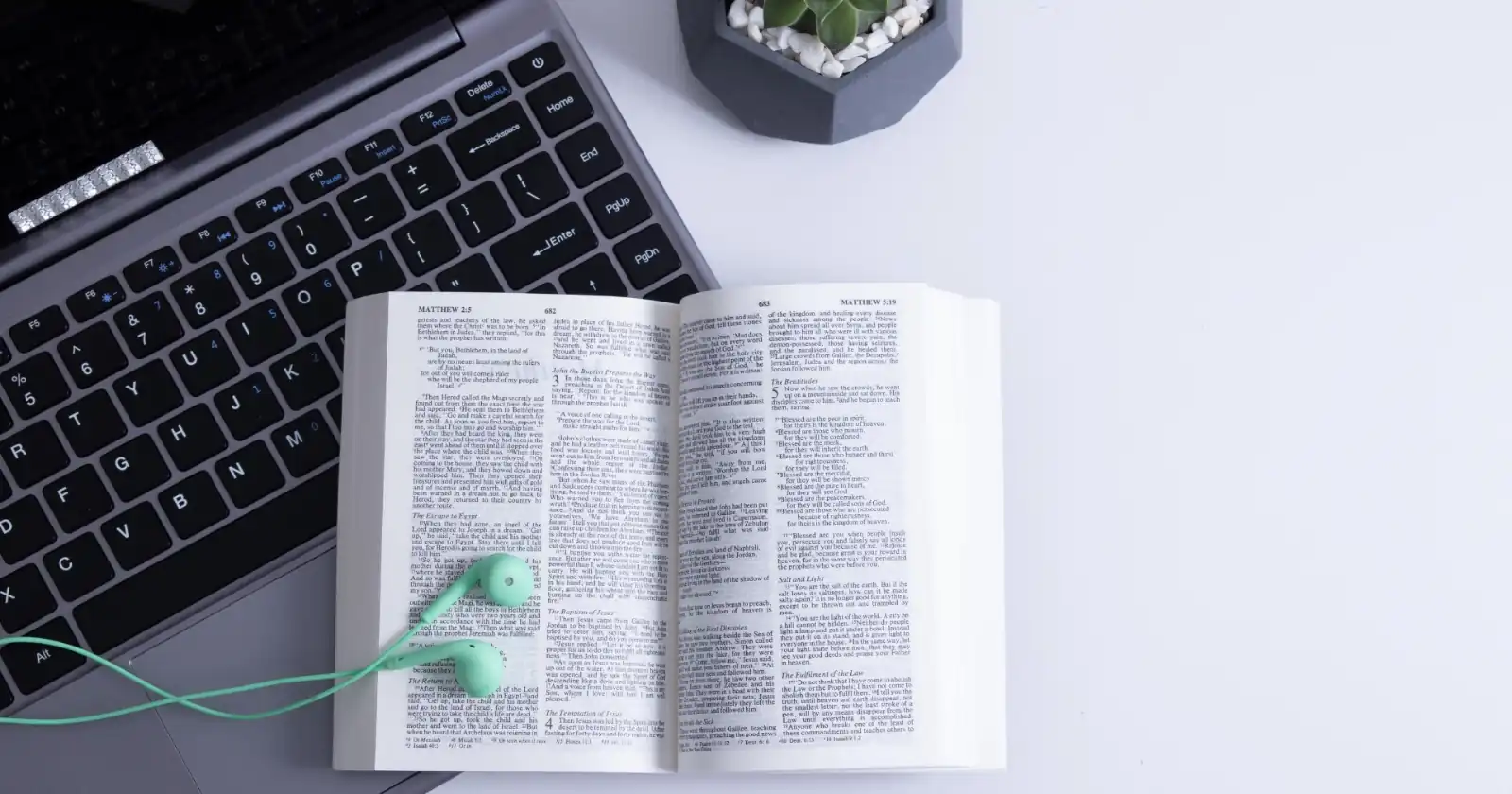 Open Bible turned to Matthew 5 resting on a laptop keyboard with green earbuds on the page