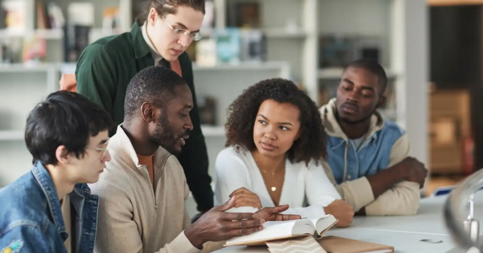 Small group leader talking with four adults around a table with an open Bible during a weekly discussion